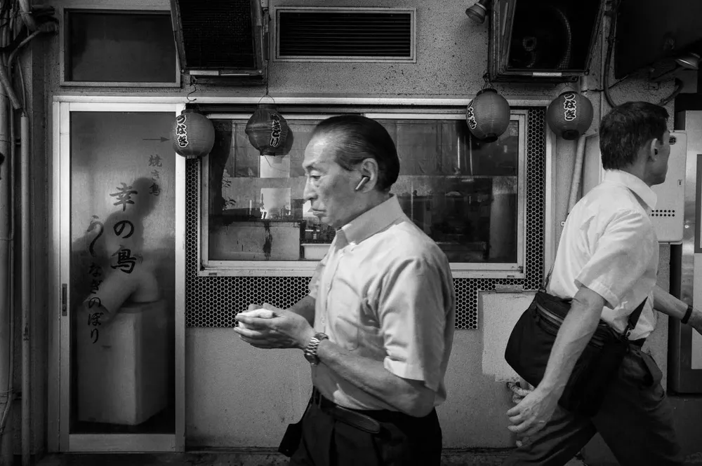 Two men stand outside a small restaurant, one holding a plate
