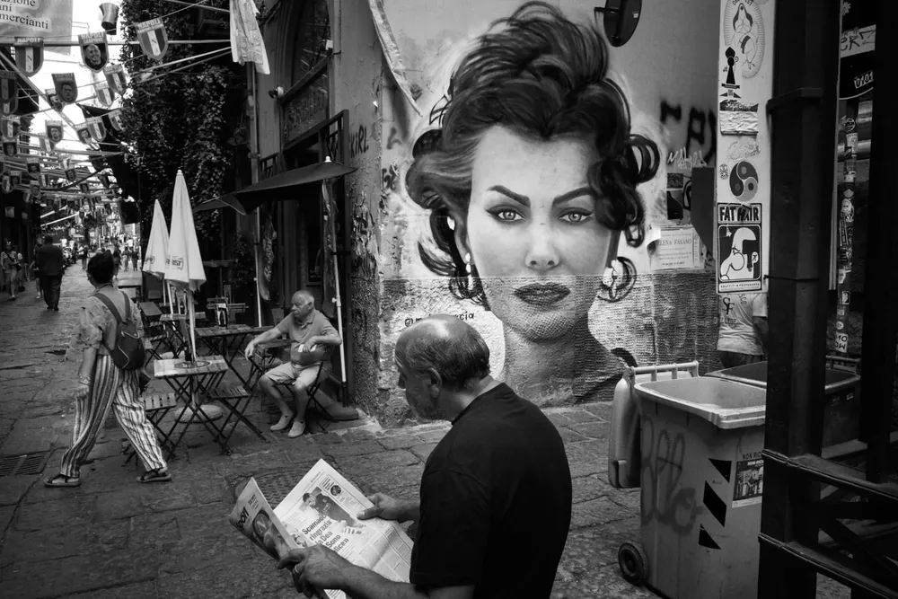 A woman turns toward the camera in a crowded narrow street