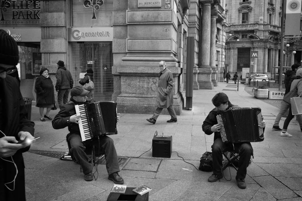 Accordion players perform beside a stone building