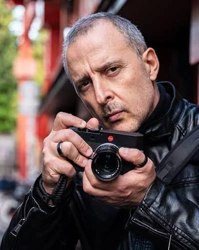Eolo Perfido holds a Leica camera beside his face